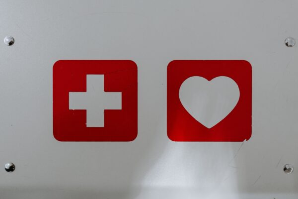A white background with two red icons: one of a white cross cut-out from a red square, and one of a white heart cut-out from a red square.